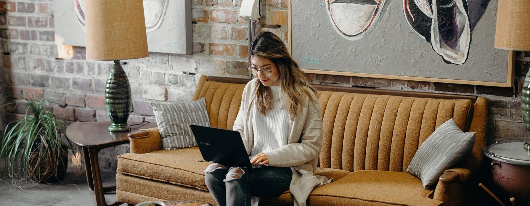 a woman sitting on a couch working on a laptop