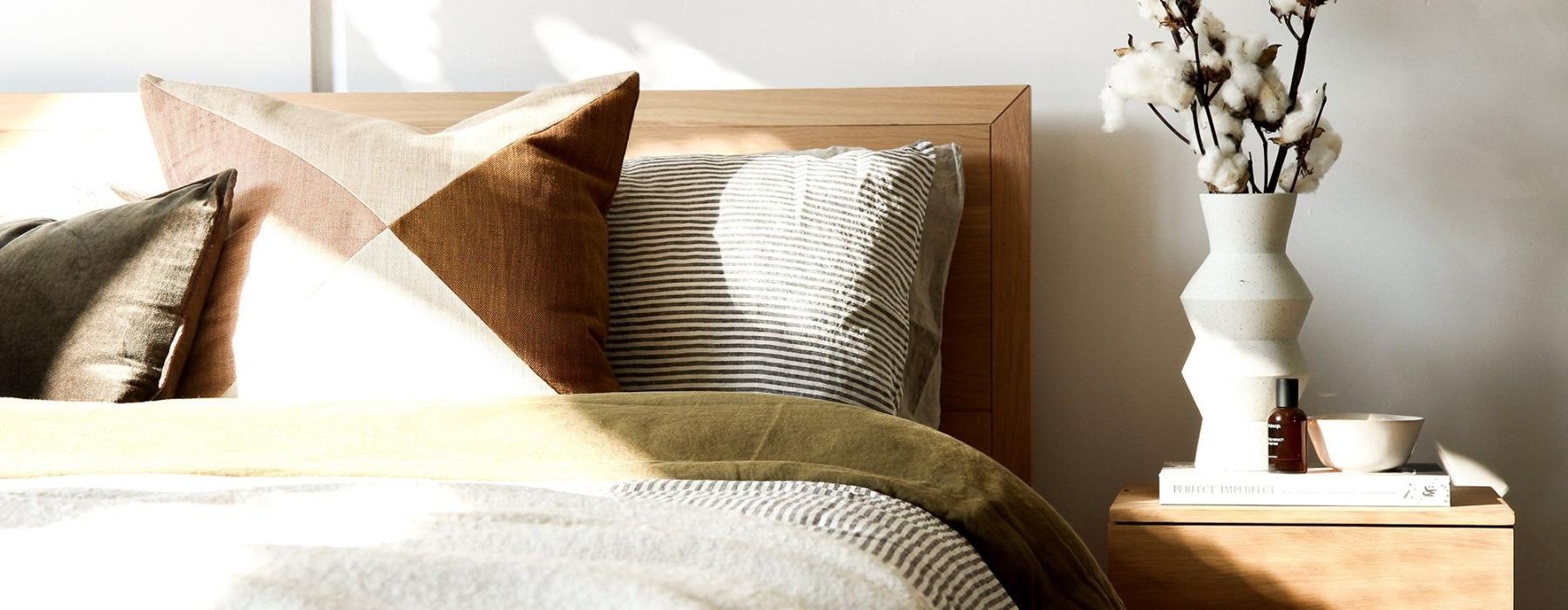 swath of sunlight shines across a well made bed and bedside table with a vase of cotton plants